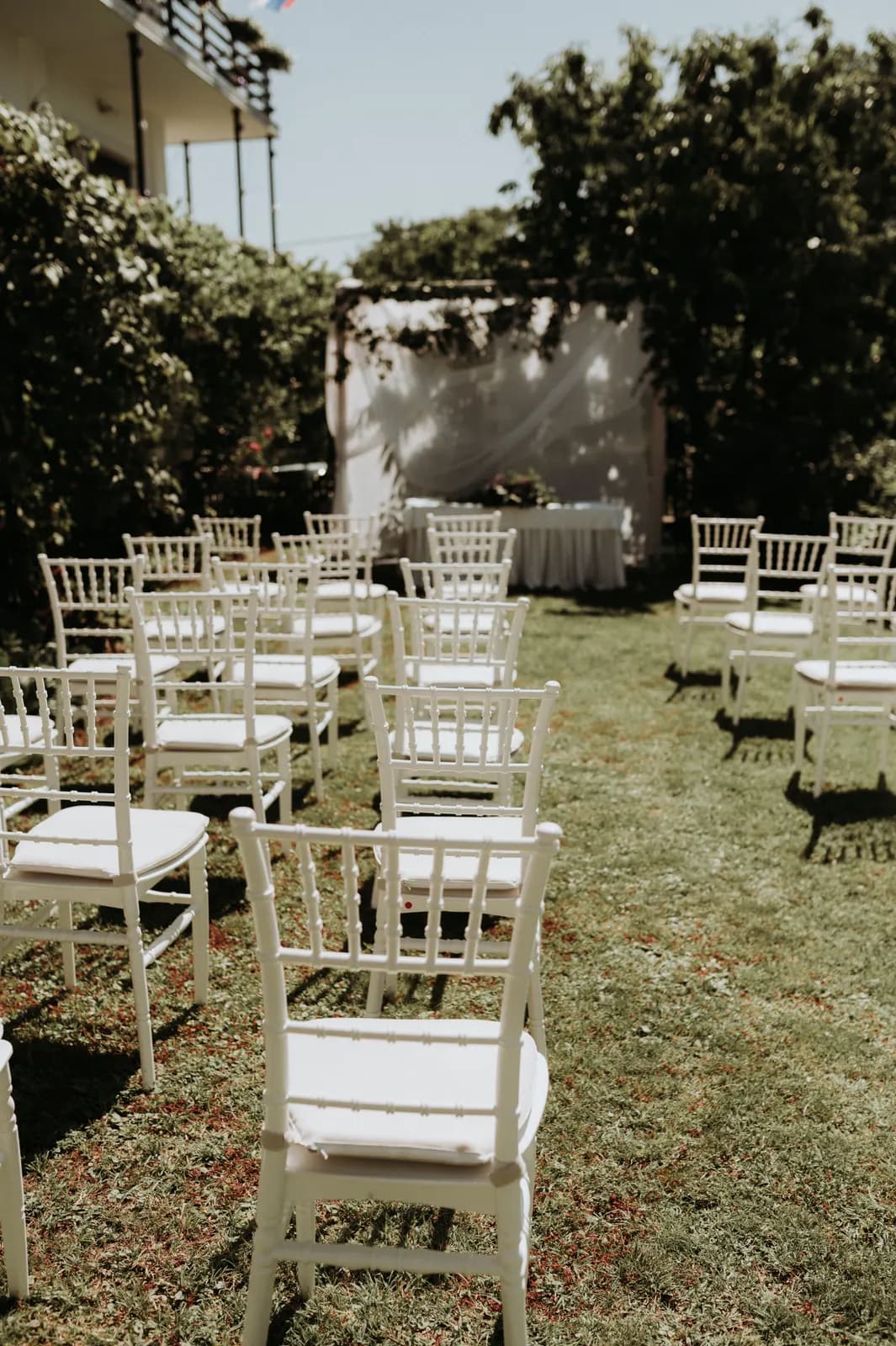 White wooden chairs set out on a lawn for an outdoor wedding ceremony