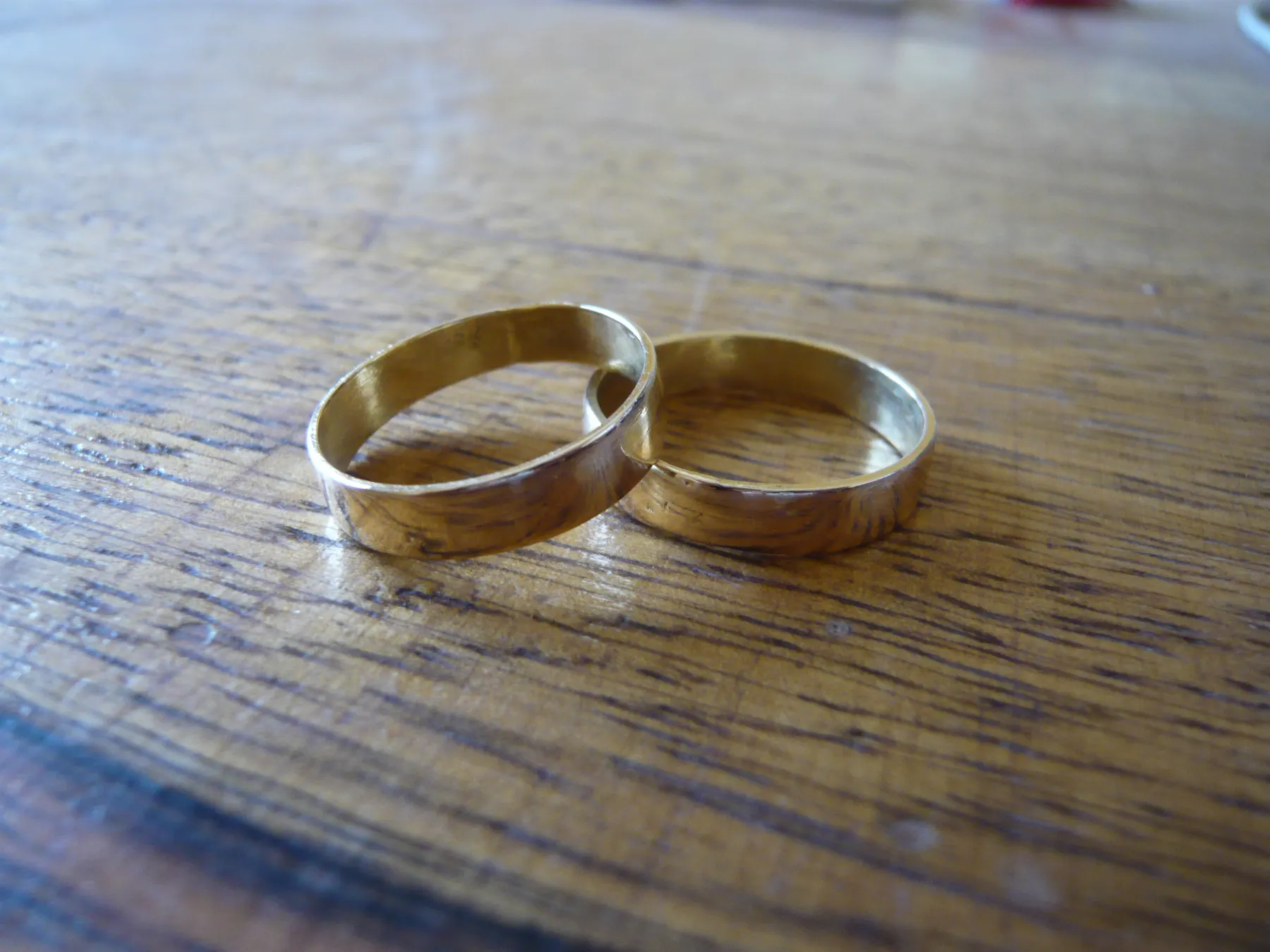 Two plain gold wedding bands on a dark wooden table