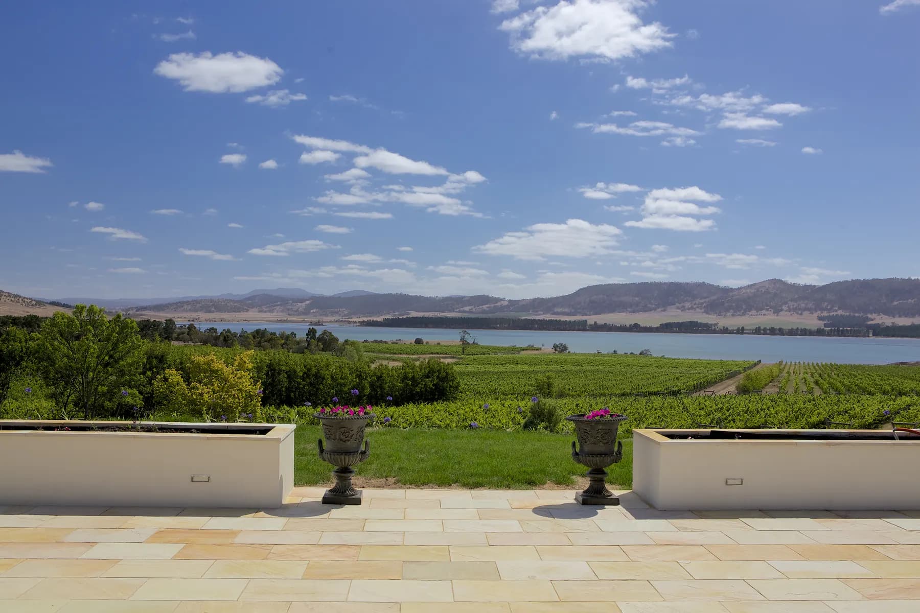 Stone terrace with urns looking out over a vineyard and a lake