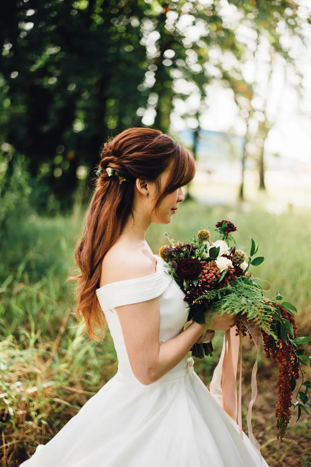 Bride in an off-shoulder dress holding a deep red and green bouquet