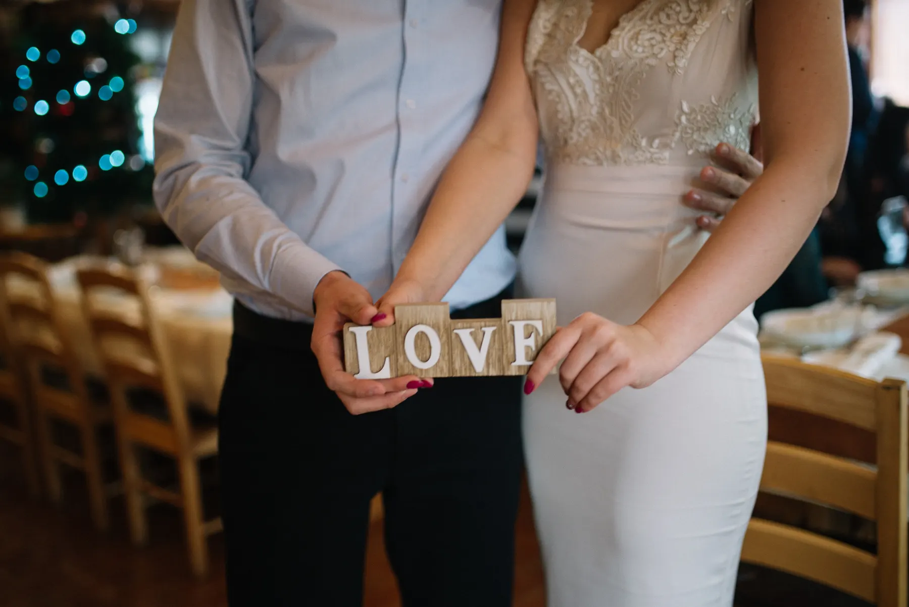 Couple holding a small wooden sign that reads love at their reception